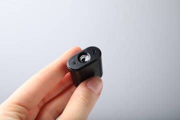 Fototapeta premium Woman holding modern hidden spy camera on light grey background, closeup