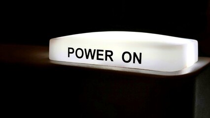 Photo of a vividly illuminated “POWER ON” button glows brightly against a dark, shadowy...