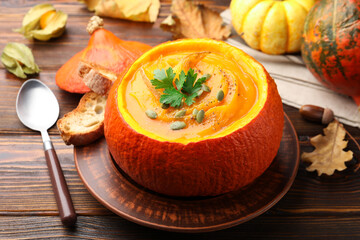 Tasty pumpkin cream soup with seeds and parsley served in pumpkin on wooden table, closeup