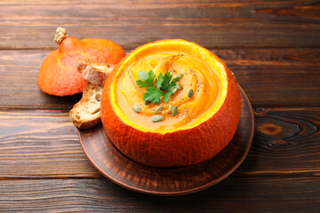 Tasty pumpkin cream soup with seeds and parsley served in pumpkin on wooden table, closeup