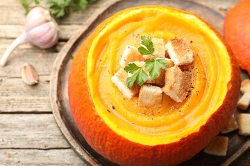 Tasty pumpkin cream soup with croutons and parsley served in pumpkin on wooden table, above view