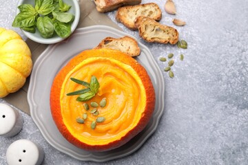 Tasty pumpkin cream soup with seeds and basil served in pumpkin on grey table, flat lay