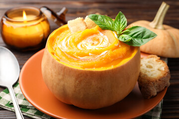 Tasty pumpkin cream soup with basil and croutons served in pumpkin on wooden table, closeup