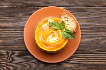 Tasty pumpkin cream soup with basil and croutons served in pumpkin on wooden table, top view