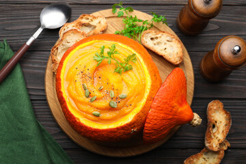 Tasty pumpkin cream soup with parsley and seeds served in pumpkin on wooden table, flat lay