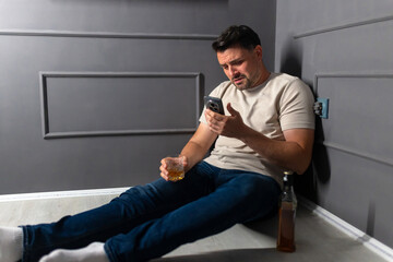 Man struggling to manage phone while sitting on floor with drink in modern interior space