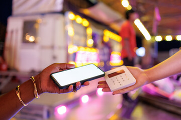 Hands using smartphone with white screen to pay on a pos terminal at night fair
