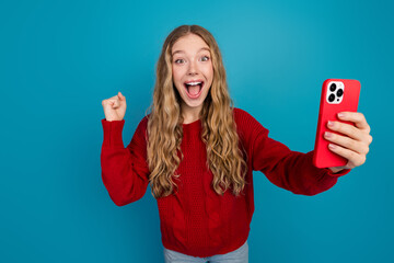 Cheerful young woman holding red smartphone, expressing excitement and joy against vibrant blue...