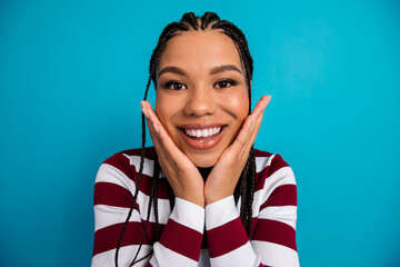 Portrait of a young woman with braids smiling against a blue background wearing a red and white...
