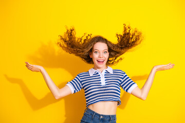 Joyful young woman in striped crop top stands against a bright yellow backdrop with hair flying
