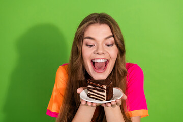 Young woman with brown hair smiles excitedly presenting a slice of chocolate cake on a plate...
