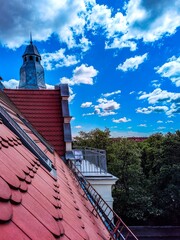 Rooftop view of a European city with a red tiled roof, tower, and vibrant blue sky
