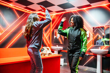 Two diverse women friends high fiving in a changing room, preparing for a go kart race, sharing excitement and fun