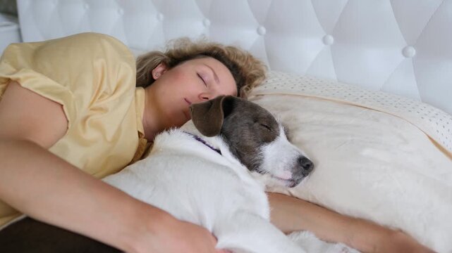 Adorable dog and its female owner sleeping together in a comfy bed at home, a woman hugging her pet while resting in the bedroom, showing a close bond and peaceful companionship