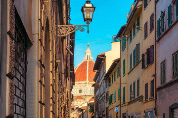Medieval narrow street in Florence city with Dome of Duomo, colorful buildings and vintage lantern, Tuscany, Italy. Dome of Cathedral of Santa Maria del Fiore in Firenze old town. Italian architecture