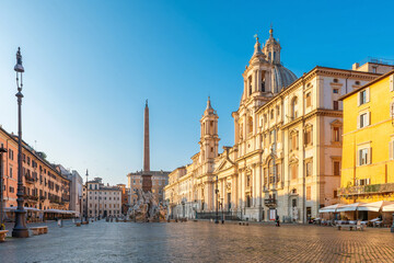 Piazza Navona with Sant'Agnese in Agone church and Fountain of the Four Rivers and obelisk surrounding by classic Roman buildings with cafes and terraces at sunrise, Rome, Italy. Italian square