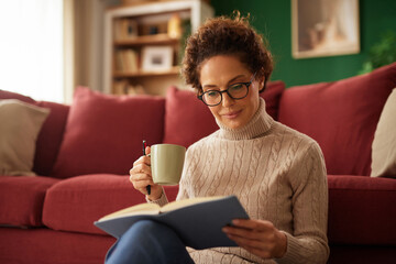 A woman relaxes on the floor of her cozy living room, reading a book while holding a mug. Soft sunlight illuminates the space, creating a warm atmosphere.