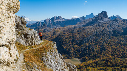 Fototapeta premium Girl with helmet and backpack admires the view from a mountain top with autumn colors in the Dolomites