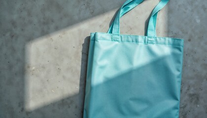 Blue tote bag resting on concrete floor with shadow. Eco friendly shopper concept. Reusable bag for grocery shopping or casual use.