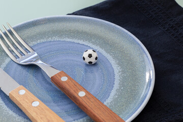 Plate with cutlery and miniature soccer ball on a domestic table. Soccer as a source of energy