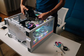 Unrecognizable computer technician installing new graphics card into modern custom-built pc with RGB lighting, enhancing gaming performance and visual experience, upgrading desktop PC.