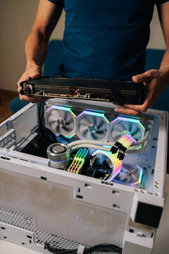 Vertical cropped shot of computer technician installing powerful new graphic card into custom-built gaming pc, featuring vibrant RGB lighting and advanced water cooling system for optimal performance.