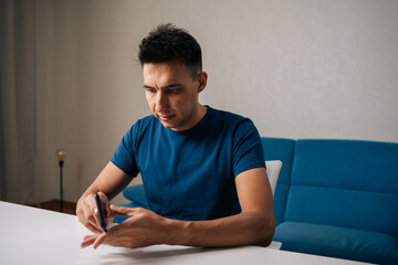 Portrait of focused young man inserting smartphone into protective case, ensuring secure fit sitting on white table at home. Concept of phone maintenance and service