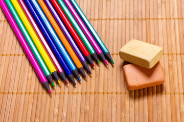 colored pencils and two erasers on a wooden surface
