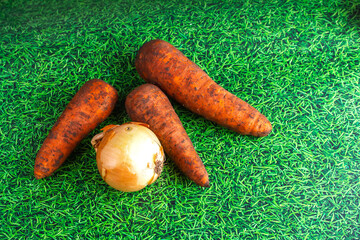 three carrots and one onion on green grass