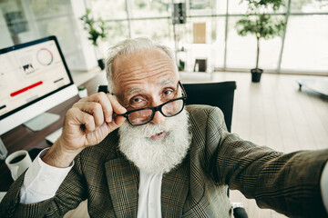 Elegant senior businessman with white beard adjusting glasses in modern office workspace showcasing confidence