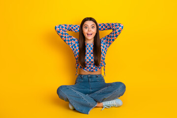 Young stylish latin teen girl with long brunette hair sits cross legged on a bright yellow...