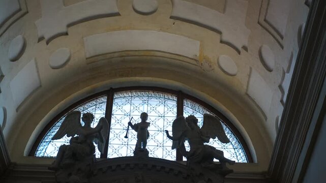 Majestic putti and angels sculptures adorning arched window in grand hall. Sunlight illuminates intricate sculptures of putti and angels gracefully positioned above an arched window