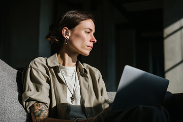 Young Caucasian woman with casual clothes and tattoos on he hands using a laptop. Female designer, freelancer working online