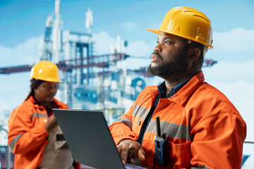 Offshore installation manager and engineer monitoring operations on oil platform deck with laptop. Drilling rig team leader and specialist reviewing energy operations using notebook