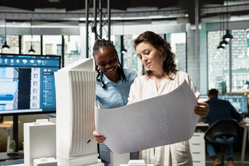 Real estate diverse team analyzing blueprints for construction layout, studying zoning regulations and engineering details with 3D models for residential project. Smart city vision for development.