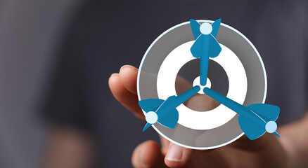 Hand holding a dartboard with three darts hitting the center, showing business, goals, target,...