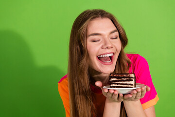 Young woman with brown hair in colorful shirt smiles while holding a slice of chocolate cake on a...