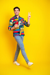 Young stylish man posing with phone and peace sign against bright yellow background for fashion and...