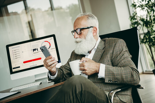 Confident senior businessman reviewing data on smartphone while enjoying coffee in elegant office setting