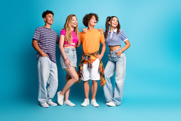 Fototapeta premium Playful group of four teens posing with energy and style as friends celebrate summer vibes against a bright blue studio backdrop