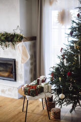 Stylish Christmas presents. Merry Christmas and Happy Holidays! Wrapped Christmas gift boxes on table at decorated xmas tree with lights in cozy room. Atmospheric winter time