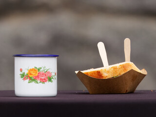 A floral enamel mug and a paper tray with a snack on a table at the Prague  Naplavka farmers market.