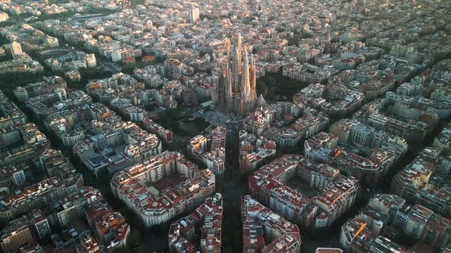 4K drone aerial view of Sagrada Familia in Barcelona at sunset, showing golden light over Eixample district and iconic grid city pattern, Catalonia, Spain