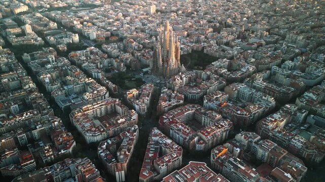 4K drone aerial view of Sagrada Familia in Barcelona at sunset, showing golden light over Eixample district and iconic grid city pattern, Catalonia, Spain