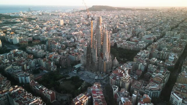 4K drone aerial view of Sagrada Familia in Barcelona at sunset, showing golden light over Eixample district and iconic grid city pattern, Catalonia, Spain