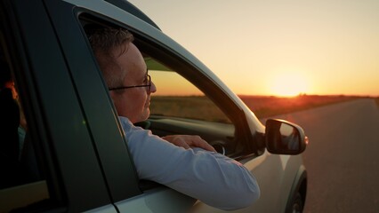 Man passenger sits in car looks out window, enjoying wind, nature at sunset. Happy family. Man woman couple enjoy car trip out of town. People travel by car, leading an active lifestyle on vacation