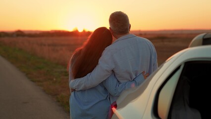 Man woman hug enjoying sunset next to car on road. Happy family. Man woman couple standing hugging enjoying car trip out of town. People travel by car, leading active lifestyle in nature on vacation
