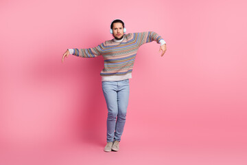 Young man wearing headphones and a patterned sweater dancing against a pink background, showcasing casual fashion and joyful expression.
