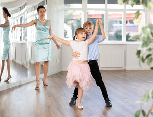 Naklejka premium Boy with girl during contemporary vigorous dancing lesson. Children rehearse rumba movement. Female teacher conducts class for students during dance workout