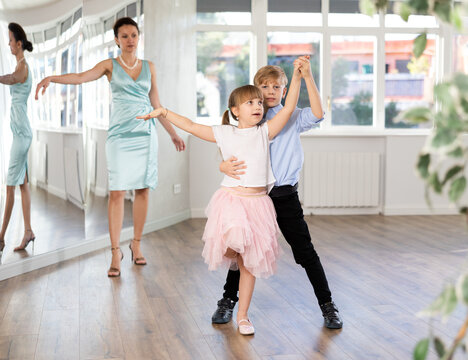 Boy with girl during contemporary vigorous dancing lesson. Children rehearse rumba movement. Female teacher conducts class for students during dance workout